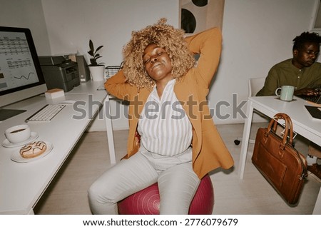 High angle shot of female worker doing fitness exercise on fitball while having break in office