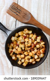 High angle shot of Fried Breakfast Potatoes in a cast iron skillet. Peppers, onions and potato cubes fill the skillet resting on a rustic farmhouse style kitchen table with a wooden fork.