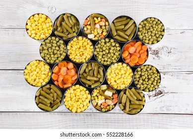 High Angle Shot Of A Group Of Canned Vegetables On A Rustic White Wood Table. Several Varieties Of Opened Cans Including, Corn, Green Beans, Peas, Carrots And Mixed Veggies.