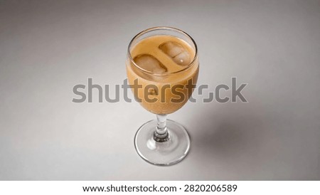 High angle shot of iced latte coffee in a glass stemware with floating ice cubes on plain background.