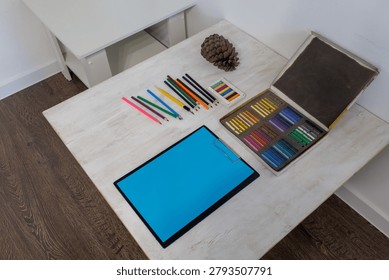 A high angle shot from the left side showing art supplies, a clipboard with blue paper, and a pine cone on a table.