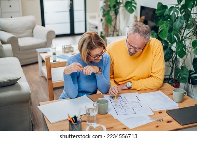 High angle shot of a married senior couple considering a blueprints of a new house property while sitting at the table with a laptop and making notes. Plan of a mortgage loan investment. Copy space. - Shutterstock ID 2234556713
