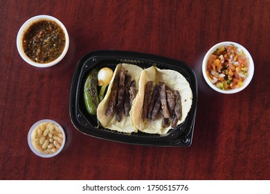 A High Angle Shot Of Mexican Beef Tacos With Fried Jalapeno, Onion In A Plastic Container Accompanied With Salsa And White Beans