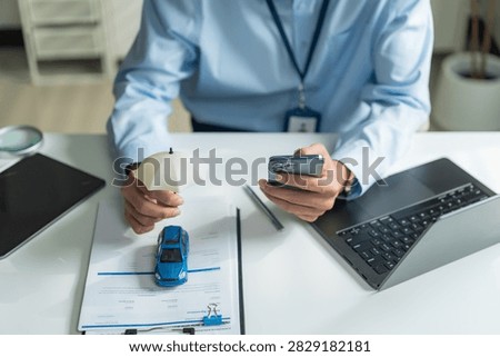 High angle shot of office worker using smartphone and holding small umbrella over toy car for auto insurance concept.