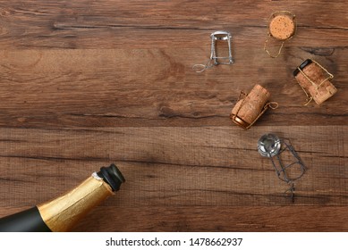 High Angle Shot Of An Ope Bottle Of Champagne With Corks In Opposite Corners Of The Frame, On A Wood Table With Copy Space.