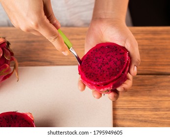 A High Angle Shot Of A Person Peeling A Red Dragon Fruit With A Spoon