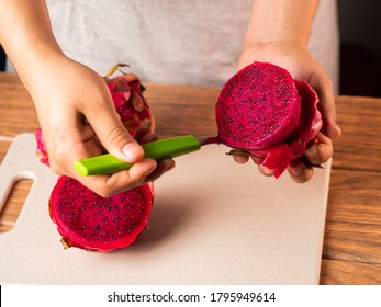 A High Angle Shot Of A Person Peeling A Red Dragon Fruit With A Spoon