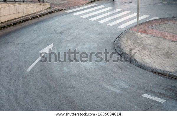 A high angle shot of a road curve\
with a white directional arrow and pedestrian\
crossing