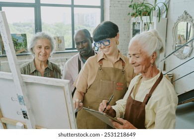 High angle shot of senior female artists smiling while her young adult teacher and biracial friends looking at her painting - Powered by Shutterstock