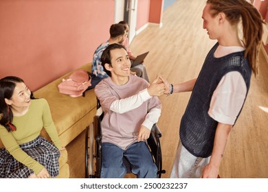 High angle shot of smiling male student with disability friendly greeting dreadlocked classmate with handshake in university hallway - Powered by Shutterstock