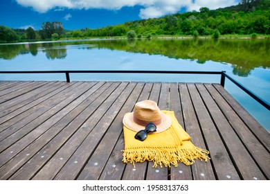 High Angle Shot Of Straw Hat And Sunglasses On The Lake Shore. Summer Vacation Concept. Vibrant Colors.