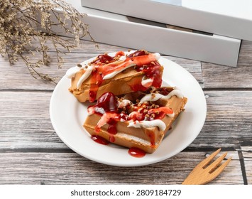 A high angle shot of two crispy waffles topped with sweet strawberry sauce and custard cream on a white ceramic plate.