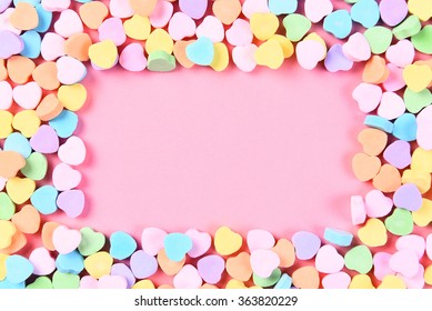 High angle shot of Valentines Day candy hearts on a pink background with copy space. The hearts form a frame around the pink background.