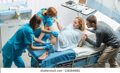 High Angle Shot of a Woman in Labor Pushes to Give Birth, Obstetricians Assisting, Spouse Holds Her Hand. Modern Maternity Hospital/ Delivery Ward with Professional Midwives. - Powered by Shutterstock