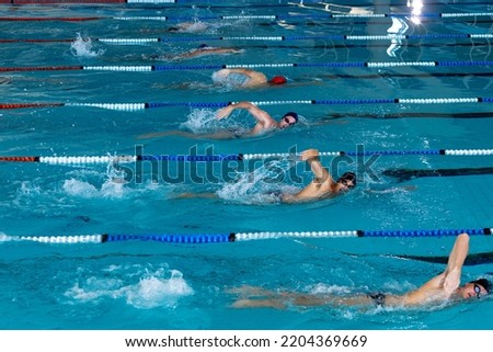 High angle side view of multi-ethnic group of male swimmers at swimming pool, racing each other in lanes, swimming crawl