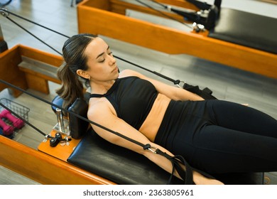 High angle of a sporty beautiful woman working out using a bed reformer while taking a pilates class for her core abs - Powered by Shutterstock