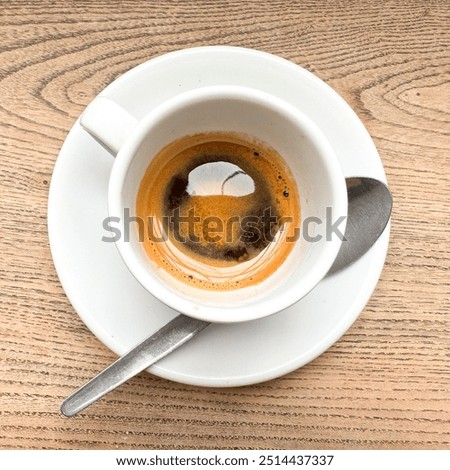 High angle square view over a delicious and beautiful expresso coffee in a white cup with a spoon. Beautiful brown foam color and aroma. Wooden table background.