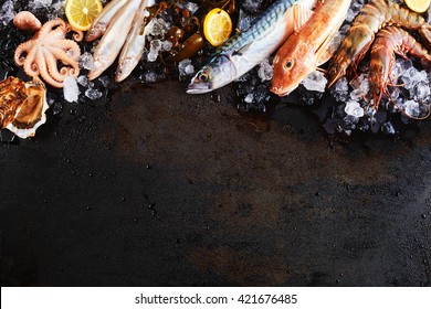 High Angle Still Life View Of Variety Of Raw Fish And Seafood Chilling On Ice With Lemon And Arranged Around Border Of Image On Rustic Wooden Table Surface With Copy Space