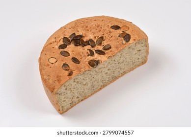 A high angle studio shot of a half cut round wheat bread loaf topped with crunchy pumpkin seeds showing the soft crumb inside on a solid white surface