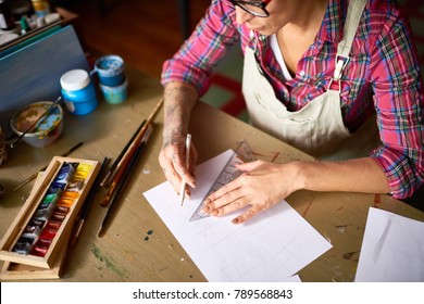 High Angle Of Tattooed Young Woman Drafting Sketch With Pencil For Art And Craft Project Sitting At Wooden Table In Workshop