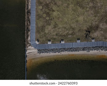 A high angle top down view of a wooden walking path and pier on Oyster Bay on Long Island, NY. Taken on a sunny day. The drone camera tilted downward.