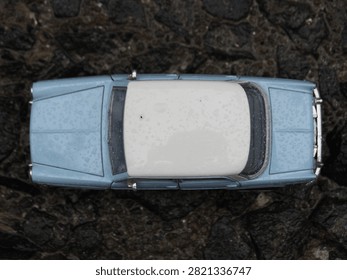 High angle top down view of two vintage miniature toy cars in blue parked on wet dark gravel