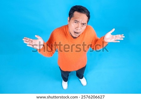 High Angle Top View Of Doubtful Young Guy Shrugging Shoulders On Blue Studio Wall