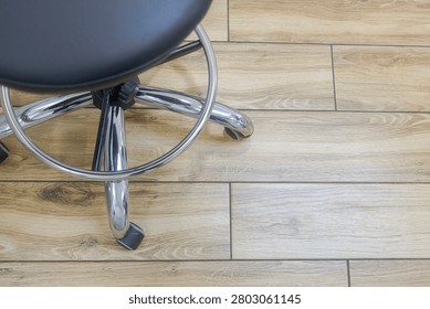 High Angle Top View of Ergonomic Medical Stool Chrome Base and Wheels on Wooden Laminate Floor in Dental Clinic