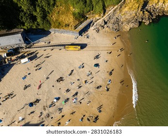 High angle top-down view over crowded resort beach, long shadows cast across golden sand by holidaymakers resting near the ocean water line