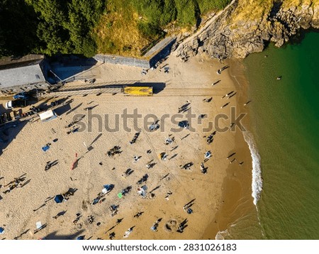 High angle top-down view over crowded resort beach, long shadows cast across golden sand by holidaymakers resting near the ocean water line