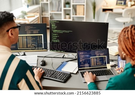 High angle of two IT developers using computers while reviewing code in office