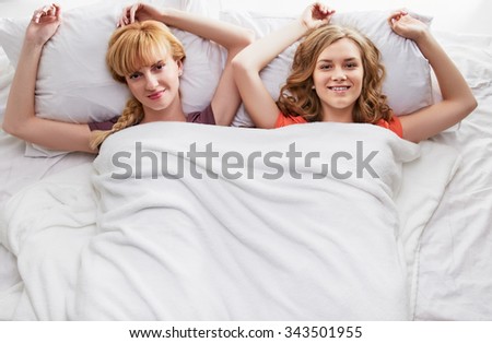 High angle of two young female friends in bed at home