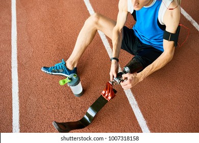 High angle of unrecognizable amputee athlete fixing prosthetic leg sitting on running track in modern stadium - Powered by Shutterstock