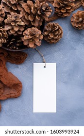 High angle vertical tabletop flat lay scene with pine cones and a small white paper card on a brown rope