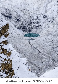 High angle vertical view of a beautiful turquoise glacial lake surrounded by snow-covered rocky mountain slopes in the Swiss Alps near Zermatt, Switzerland.