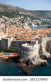 High angle vertical view of the iconic Fort Bokar, red tiled roofs of the old town, and tourists kayaking in the clear blue sea water in Dubrovnik, Croatia.