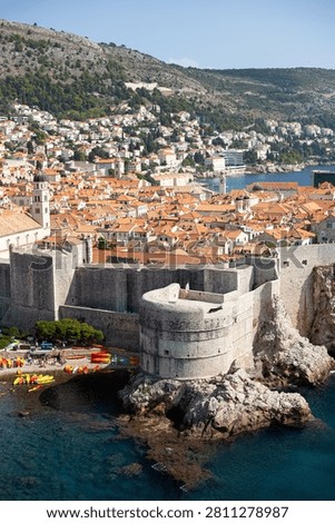 High angle vertical view of the iconic Fort Bokar, red tiled roofs of the old town, and tourists kayaking in the clear blue sea water in Dubrovnik, Croatia.