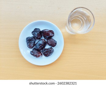 High angle view of 7 dates in a small white plate and a glass of water are on the table. The concept of breaking the fast. 