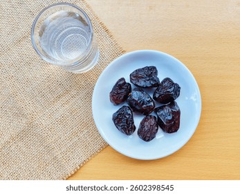 High angle view of 7 dates in a small white plate and a glass of water are on the table. The concept of breaking the fast. 