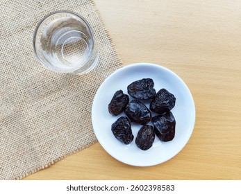 High angle view of 7 dates in a small white plate and a glass of water are on the table. The concept of breaking the fast. 