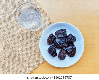 High angle view of 7 dates in a small white plate and a glass of water are on the table. The concept of breaking the fast. 