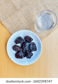 High angle view of 7 dates in a small white plate and a glass of water are on the table. The concept of breaking the fast. 