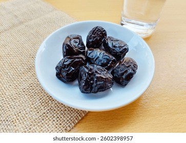 High angle view of 7 dates in a small white plate and a glass of water are on the table. The concept of breaking the fast. 