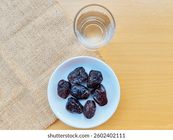 High angle view of 7 dates in a small white plate and a glass of water are on the table. The concept of breaking the fast. 