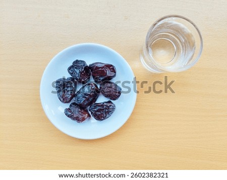 High angle view of 7 dates in a small white plate and a glass of water are on the table. The concept of breaking the fast. 