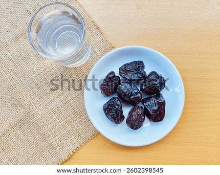 High angle view of 7 dates in a small white plate and a glass of water are on the table. The concept of breaking the fast. 