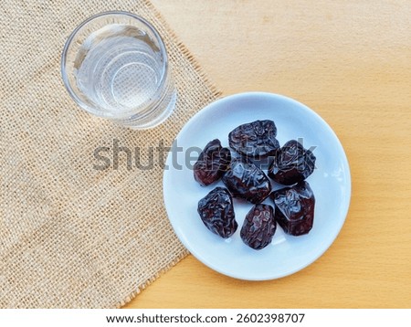 High angle view of 7 dates in a small white plate and a glass of water are on the table. The concept of breaking the fast. 