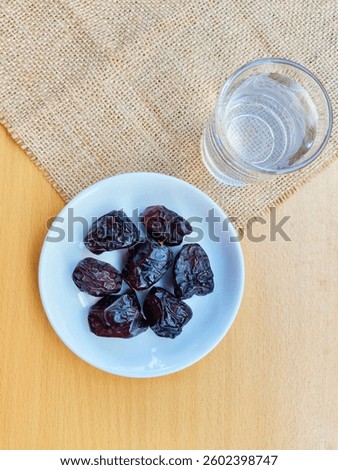 High angle view of 7 dates in a small white plate and a glass of water are on the table. The concept of breaking the fast. 