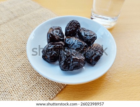 High angle view of 7 dates in a small white plate and a glass of water are on the table. The concept of breaking the fast. 