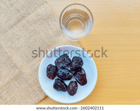 High angle view of 7 dates in a small white plate and a glass of water are on the table. The concept of breaking the fast. 